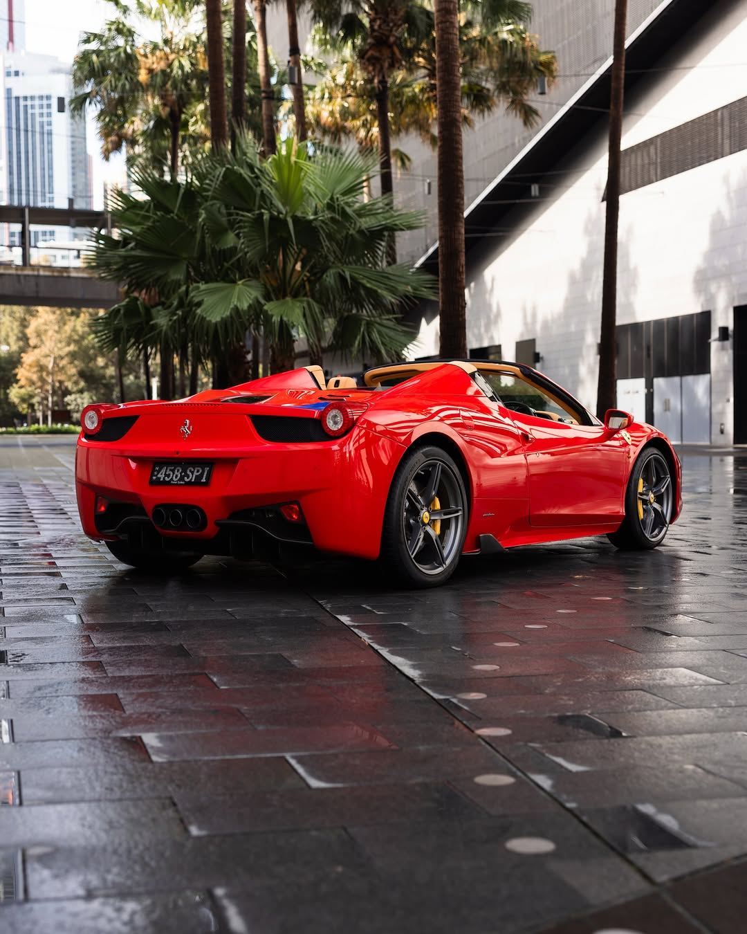Red Ferrari 458 Spider from the rear three-quarter on a wet plaza