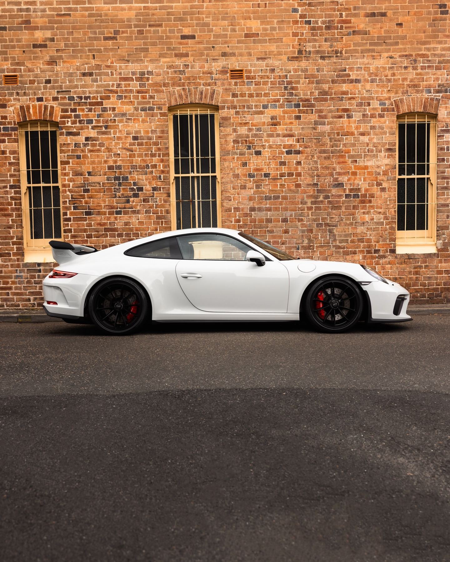 White Porsche 991 GT3 in side profile against a brick warehouse