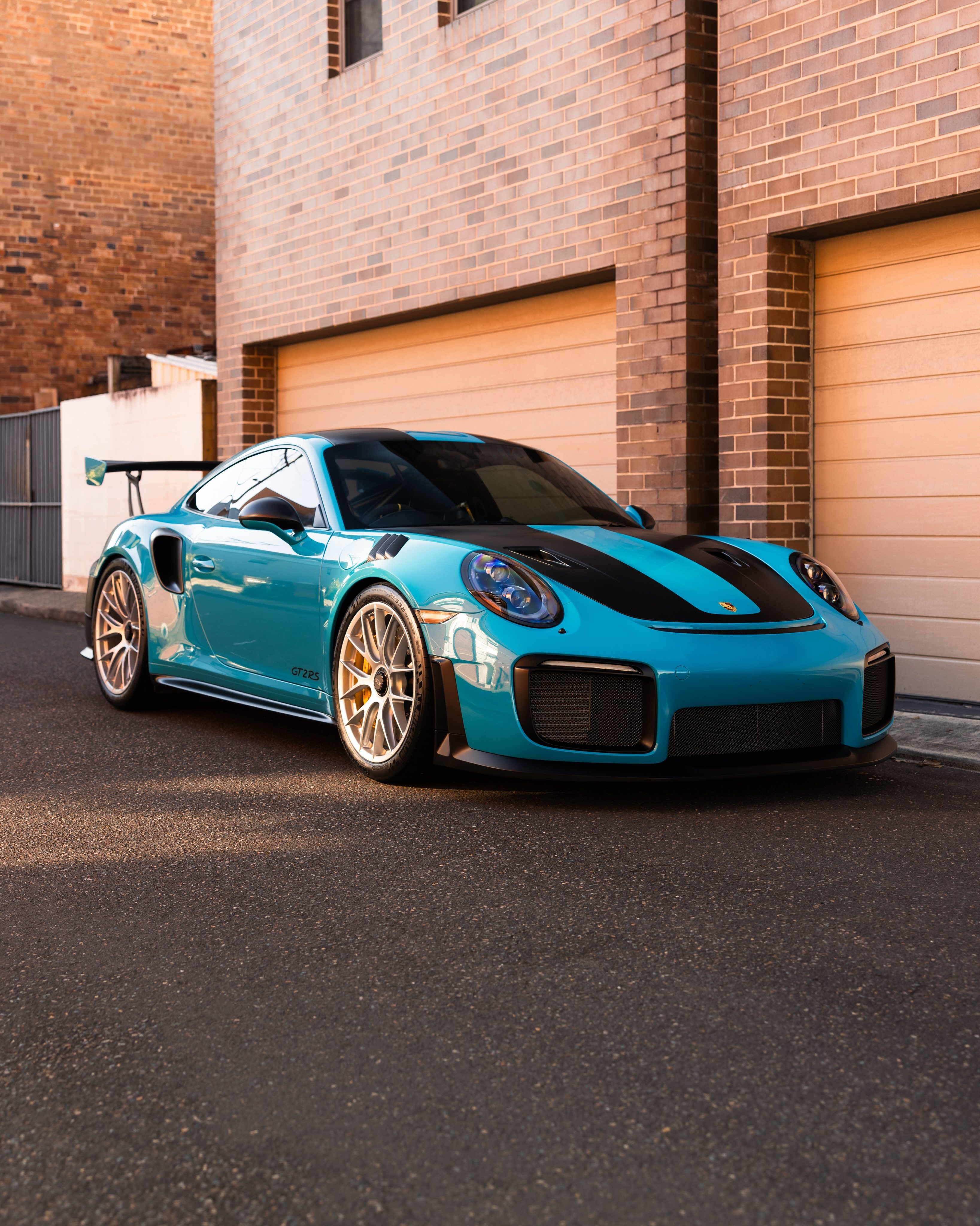 Miami Blue Porsche 911 GT2 RS in front of brick garages