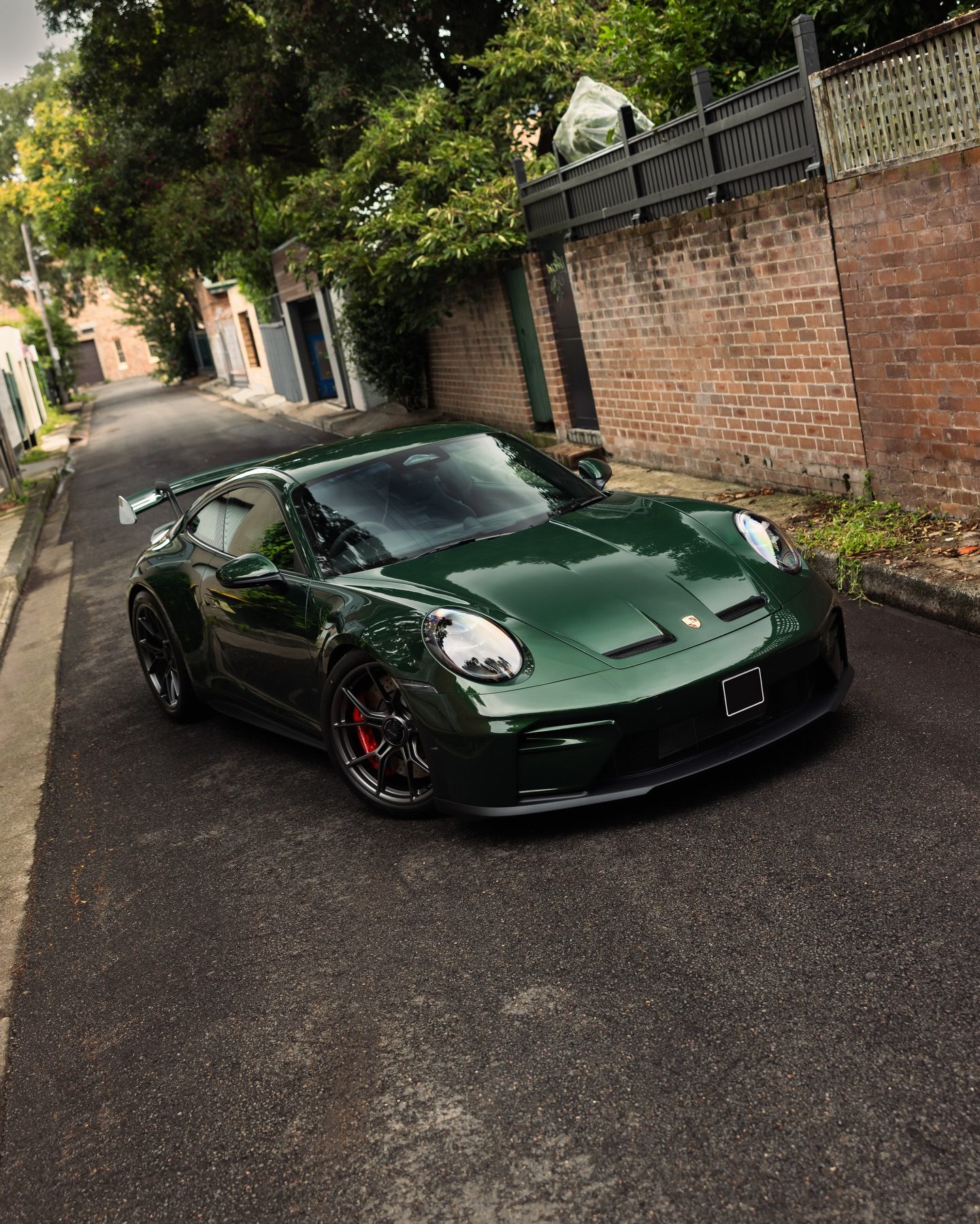 Oak Green Neo Porsche 992.2 GT3 from the front three-quarter in a lane between brick walls and trees